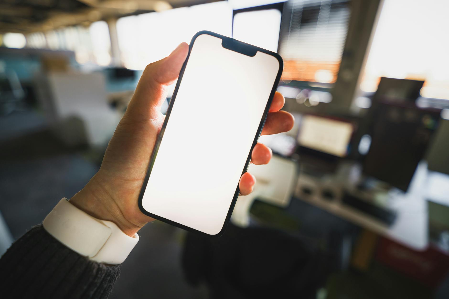 Dłoń trzyma smartfon z pustym ekranem w biurowym otoczeniu