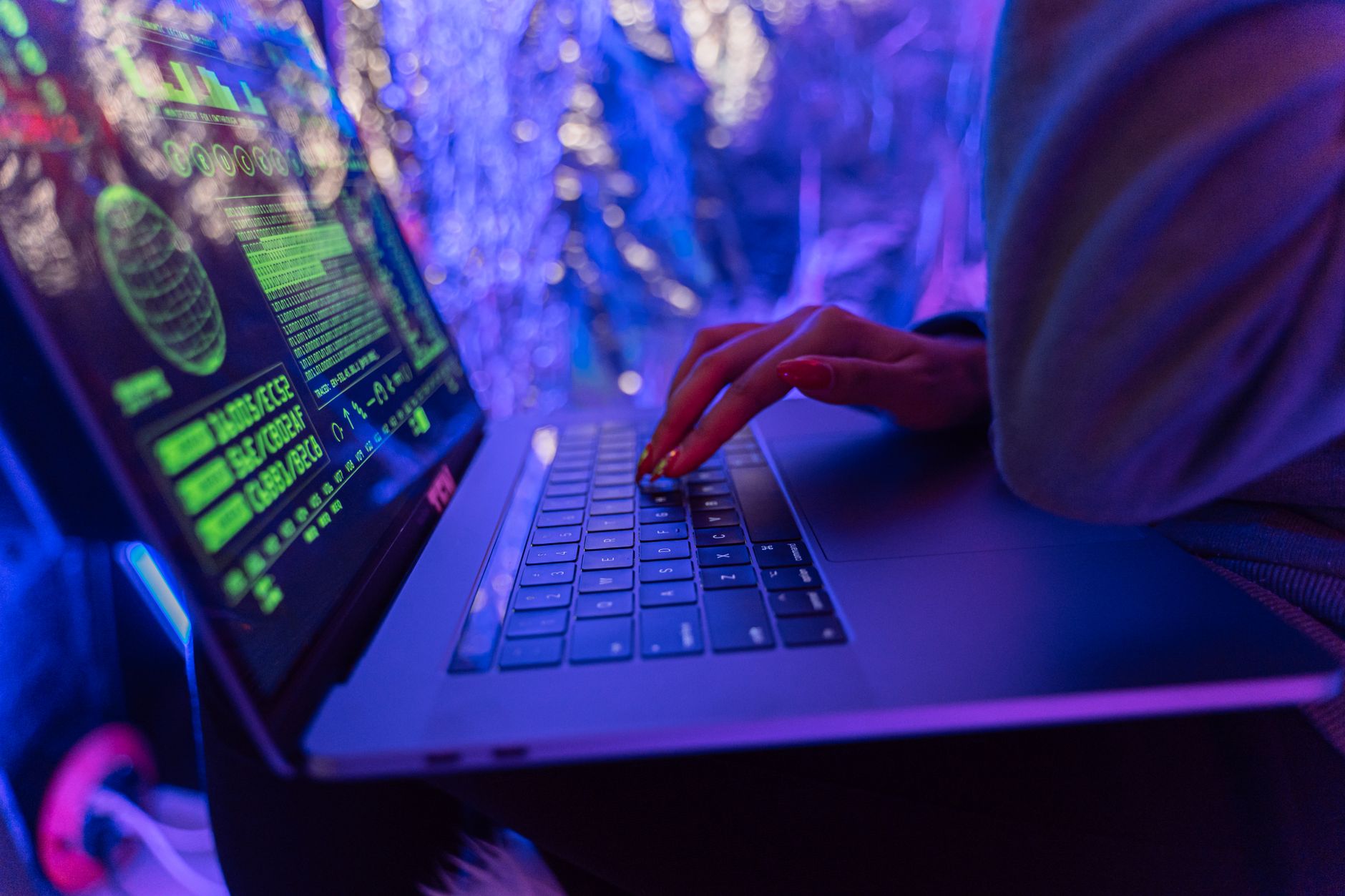 Dłonie piszące na laptopie z grafikami cyberbezpieczeństwa w fioletowym świetle