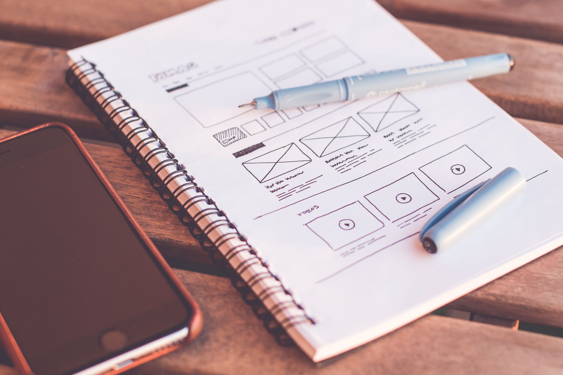 Notatnik z szkicami wireframe i smartfon na drewnianym biurku Notatnik z szkicami wireframe i smartfon na drewnianym biurku